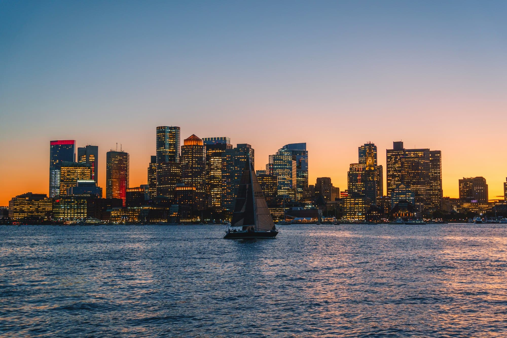 Sailboat on Boston Harbor in front of the downtown skyline at sunset